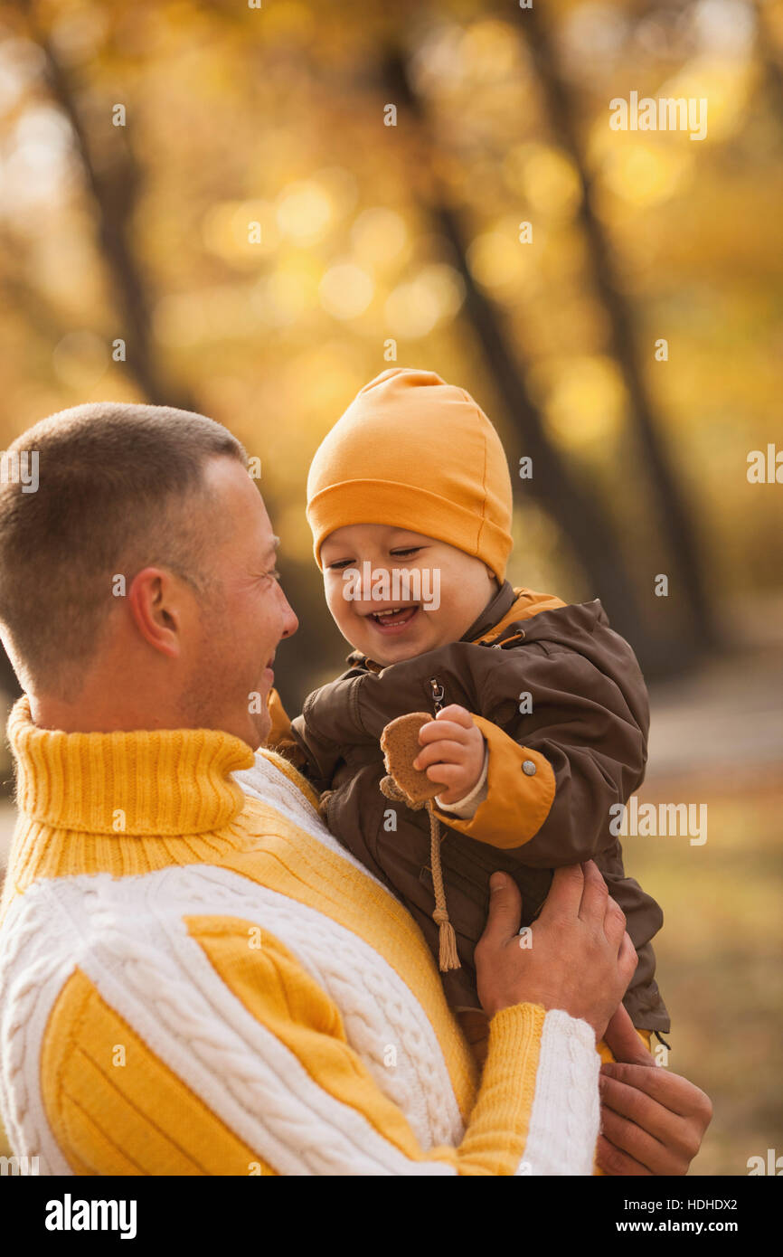 Allegro baby boy essendo portati dal padre al parco durante l'autunno Foto Stock