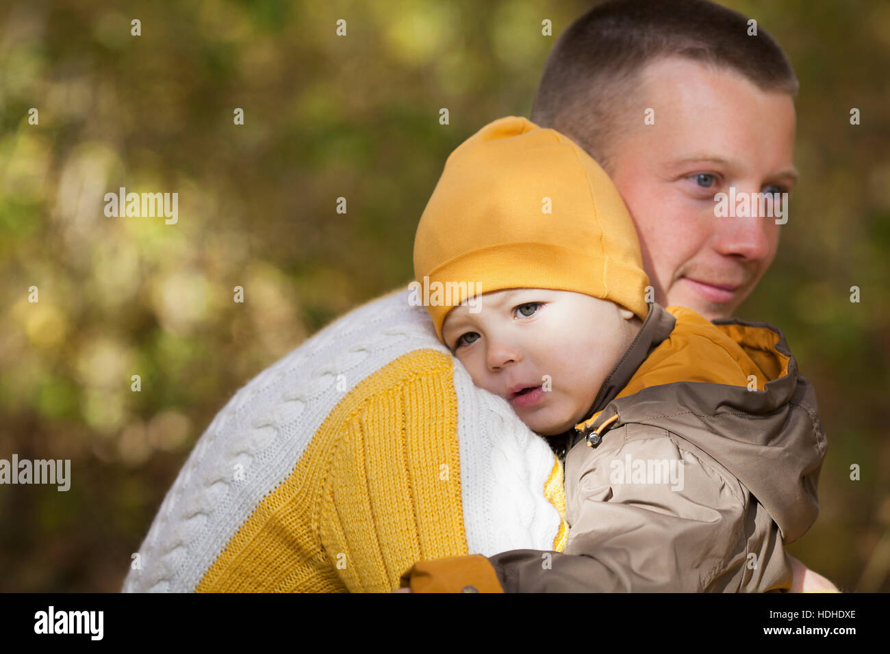 Carino baby boy essendo portati dal padre premuroso al parco durante l'autunno Foto Stock