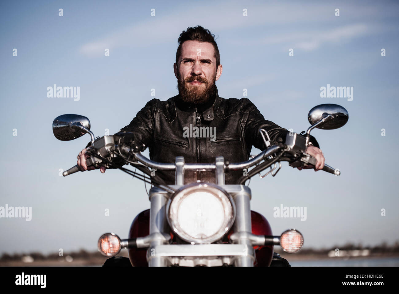 Ritratto di fiducioso biker seduto sul motociclo contro sky Foto Stock