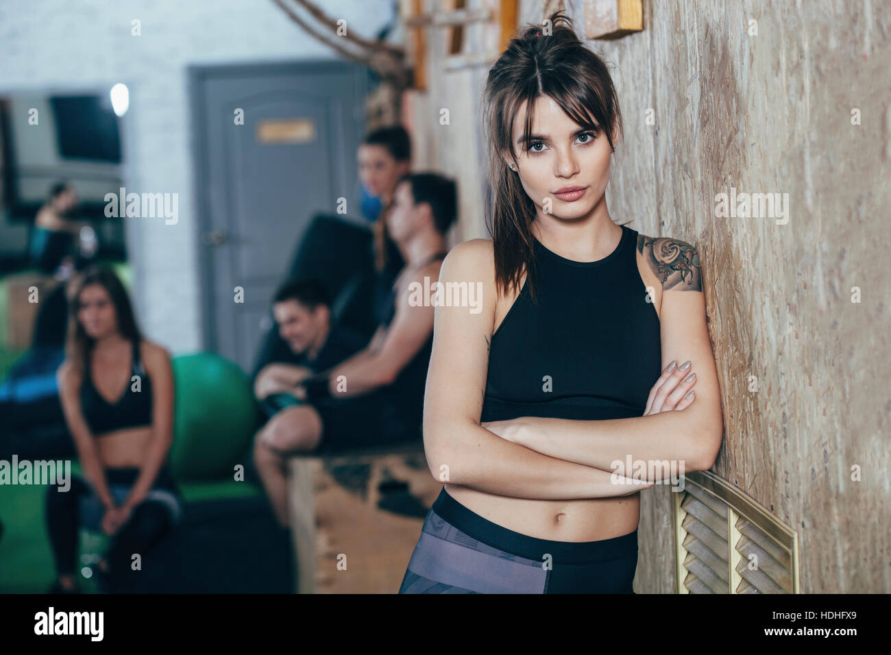 Ritratto di fiducioso atleta femminile in piedi con le braccia incrociate con gli amici in background a health club Foto Stock