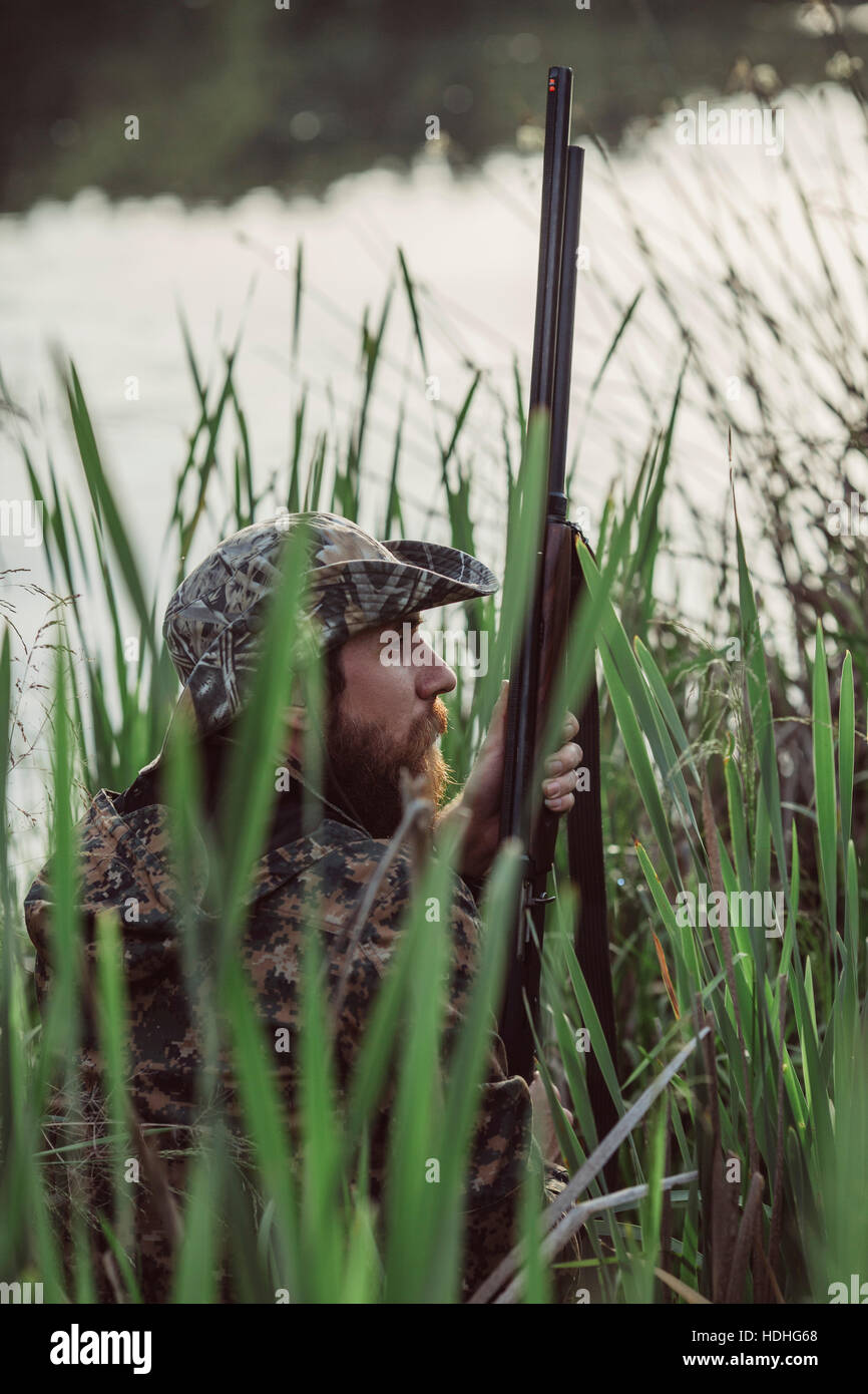 Vista laterale del cacciatore seduto in mezzo di erba a lakeshore Foto Stock