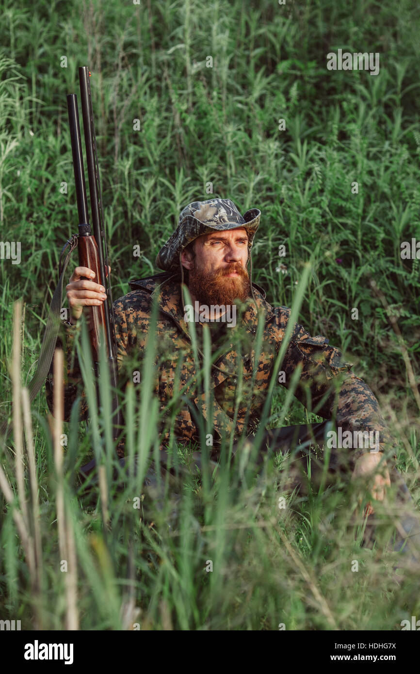 Hunter fucile di contenimento mentre è seduto sul campo erboso Foto Stock