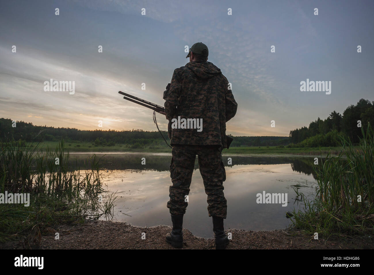Vista posteriore del cacciatore in piedi sul lungolago durante il tramonto Foto Stock