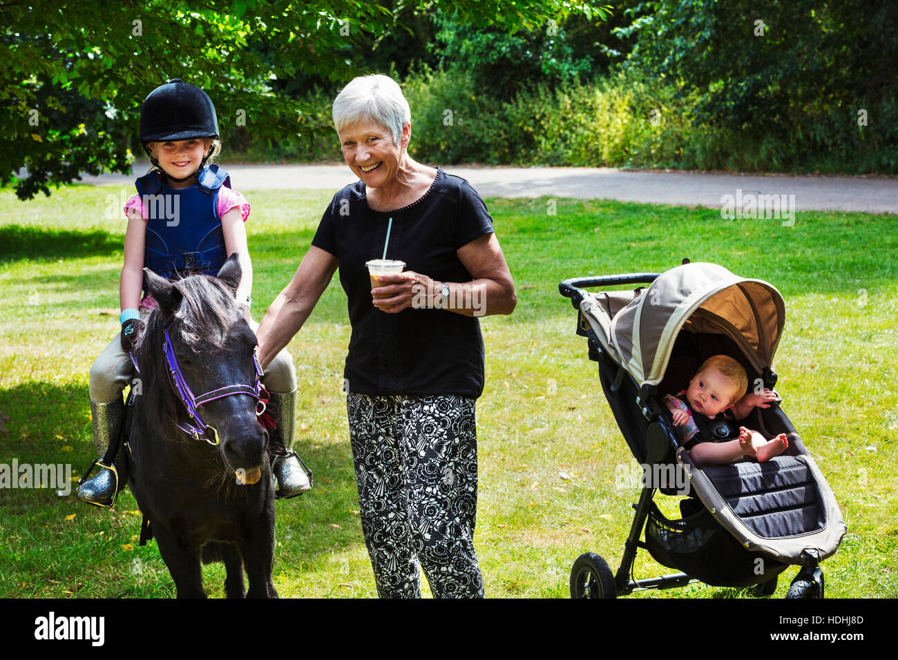 Donna, bambino nel passeggino e ragazza bionda indossando riding hat seduto su un pony. Foto Stock