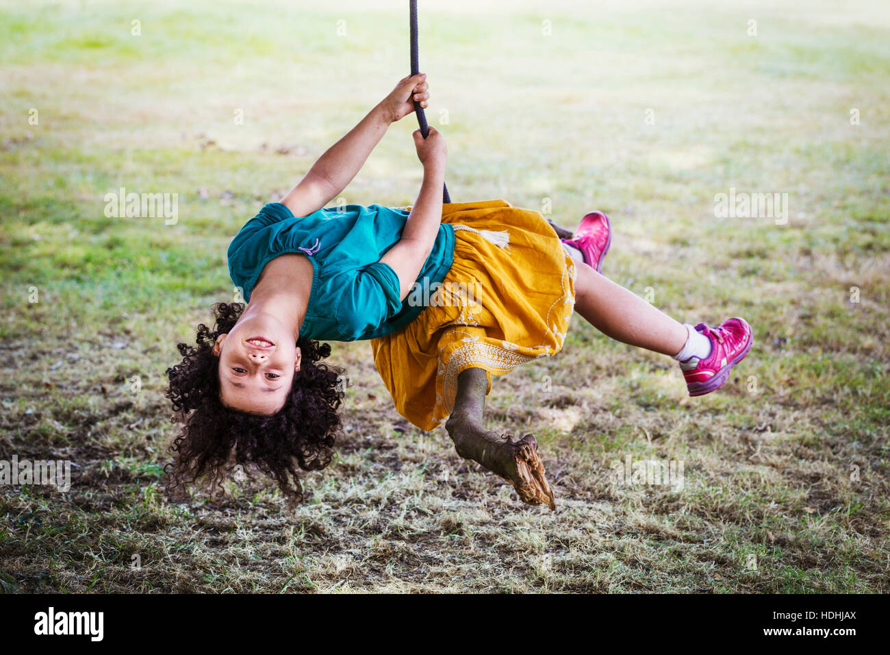 Ragazza seduta su un albero oscillante, capovolto, sorridente alla fotocamera. Foto Stock