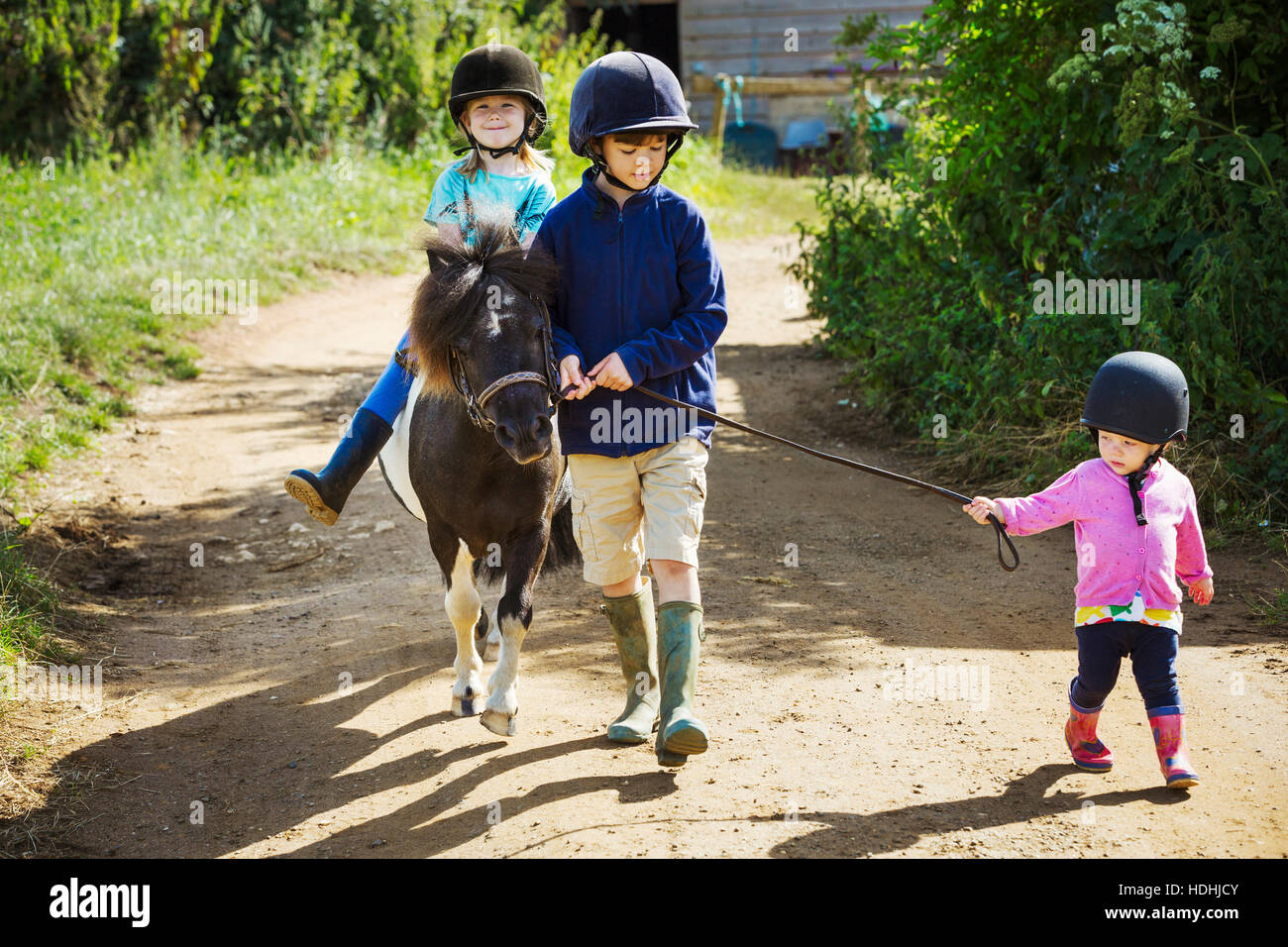 Un ragazzo, un bambino e una ragazza a cavallo di un pony su un percorso sterrato. Foto Stock