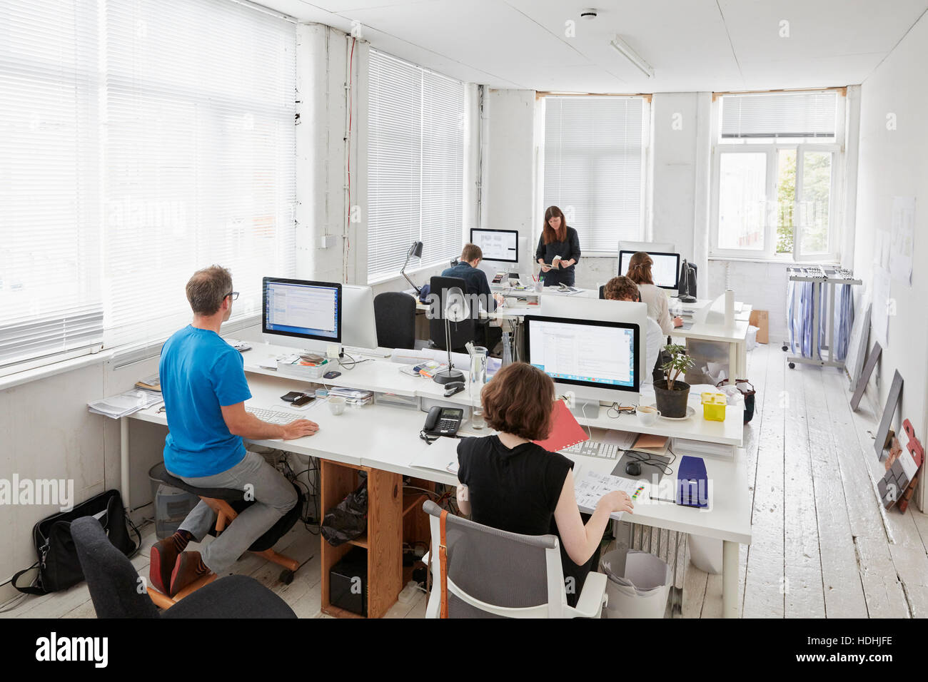 Un ufficio moderno, stazioni di lavoro per il personale. Vista in elevazione di sei persone seduto alla scrivania. Un uomo con un design ergonomico kneeler sedia. Foto Stock