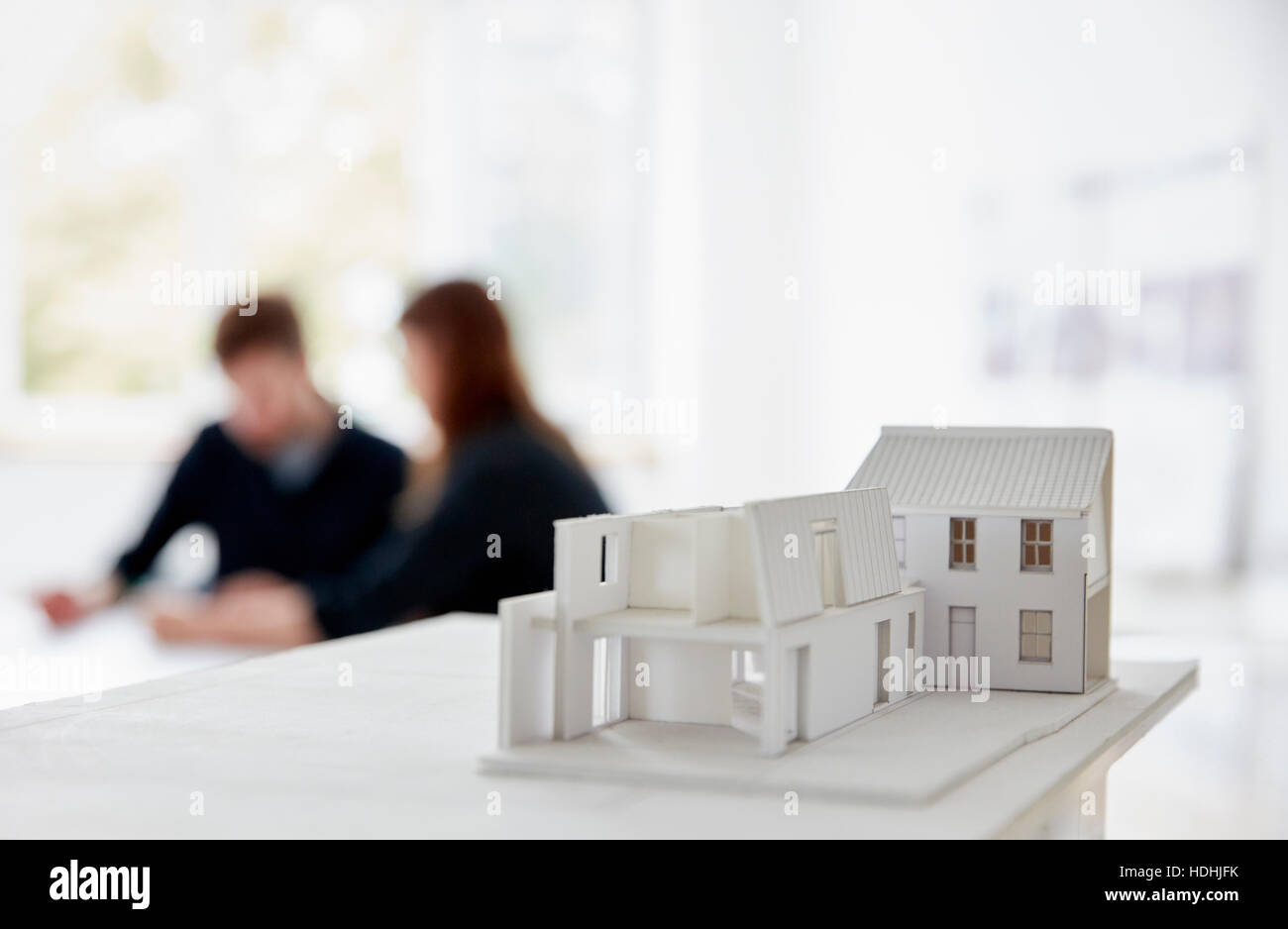Architetto ha il modello di un edificio con due persone in occasione di una riunione fuori fuoco in background. Comunicazione. Foto Stock