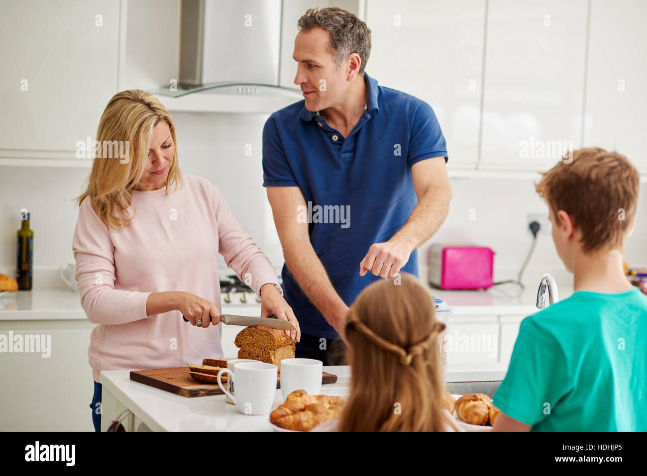 Una famiglia di quattro persone, genitori e due bambini prepara la colazione in cucina. Foto Stock