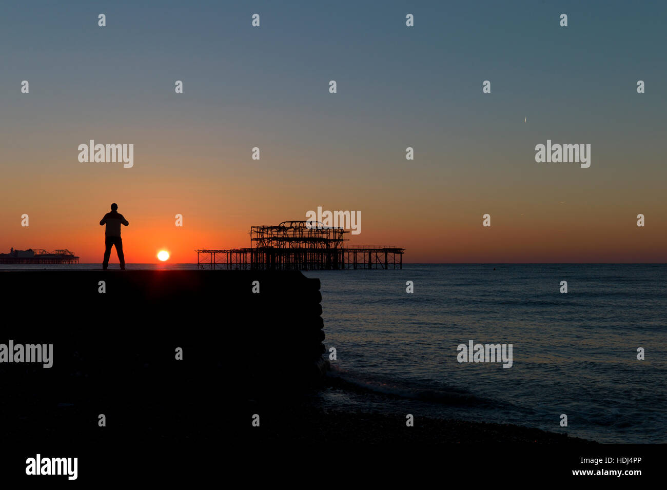 Stagliano uomo in piedi su groyne guardando sunrise tra banchine di Brighton Foto Stock
