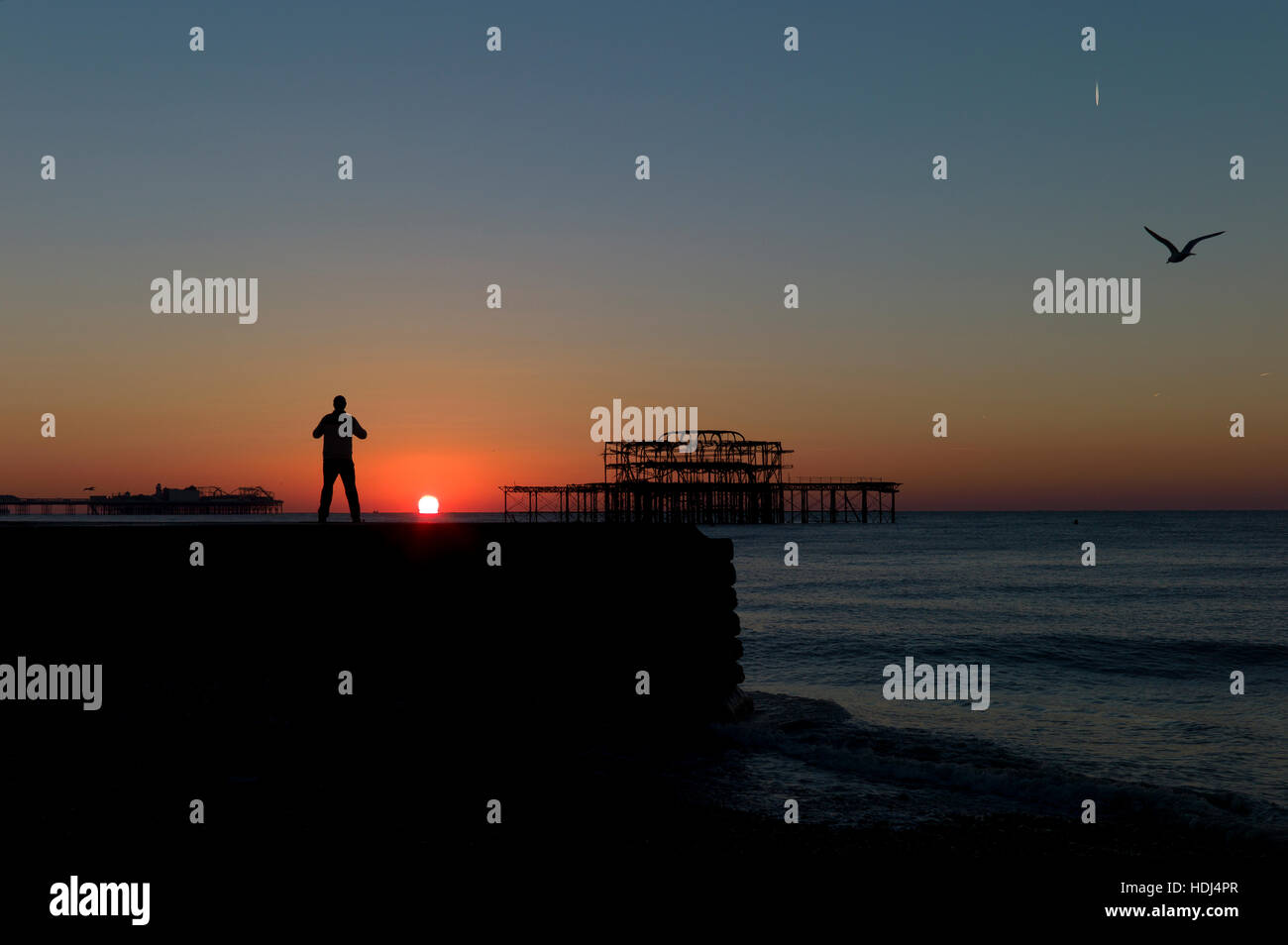 Stagliano uomo in piedi su groyne guardando sunrise tra banchine di Brighton Foto Stock