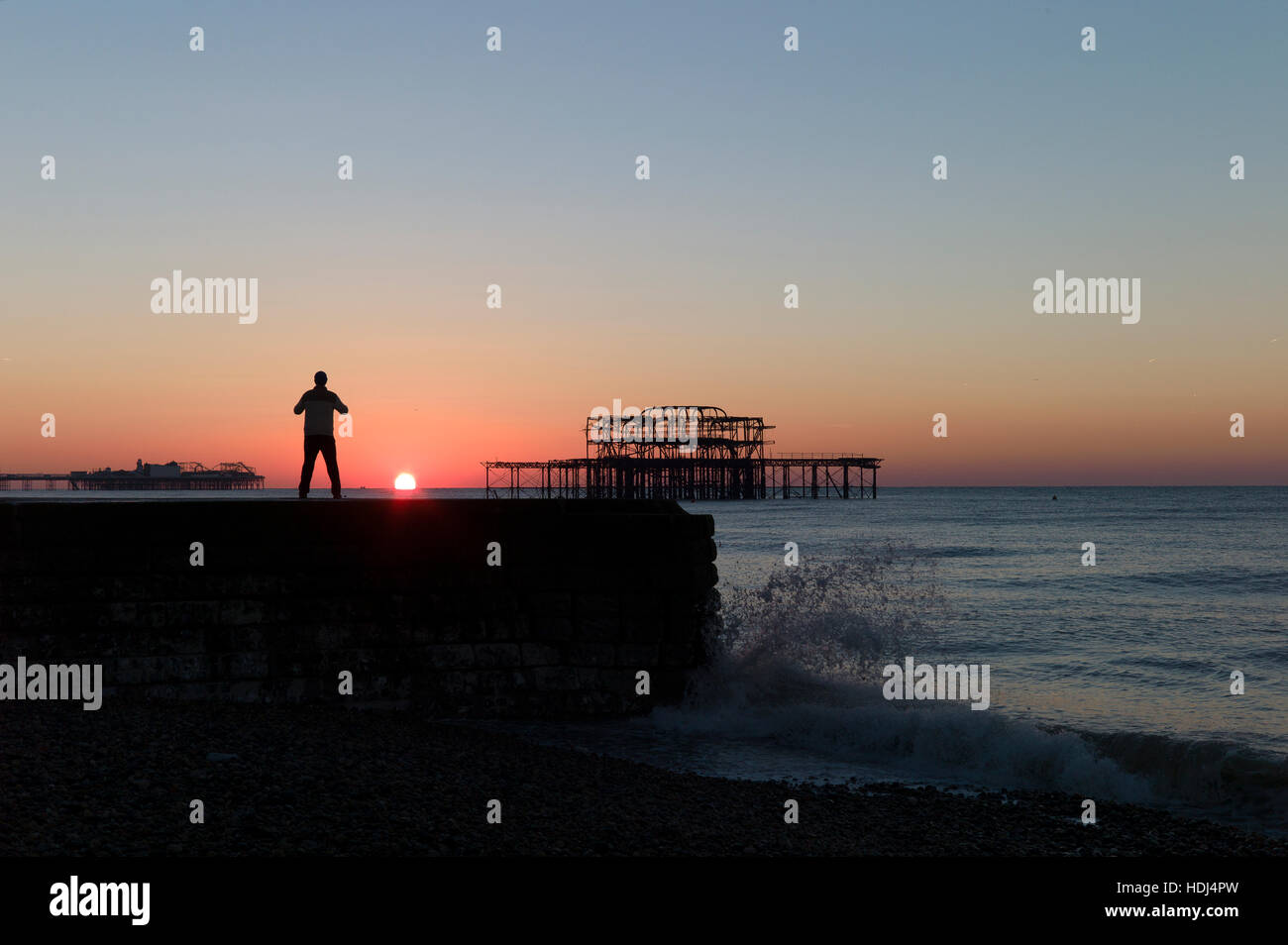 Stagliano uomo in piedi su groyne guardando sunrise tra banchine di Brighton Foto Stock
