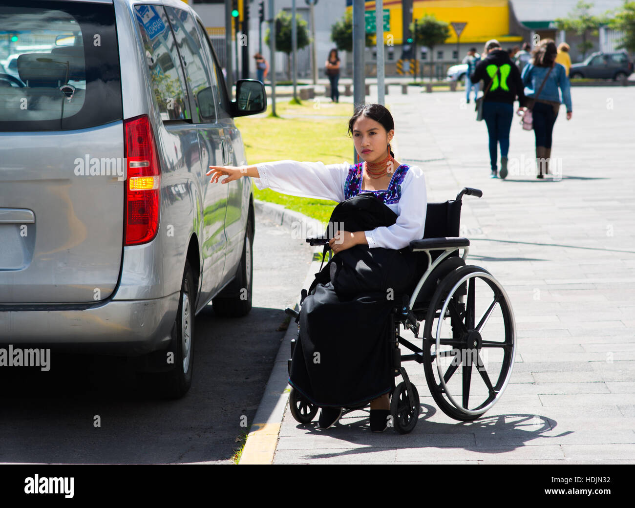 Bruna giovane donna seduta in carrozzella sorridente con atteggiamento positivo, tenendo fuori il braccio in cerca di taxi, all'aperto, ambiente fisico il concetto di recupero Foto Stock