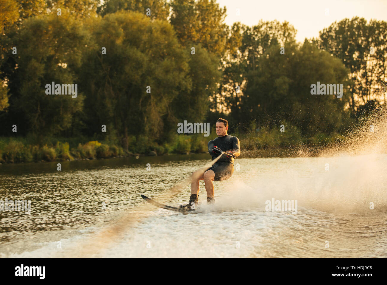 Colpo all'aperto dell'uomo Wakeboard sul lago al tramonto. Sci d'acqua sul lago dietro una barca. Foto Stock