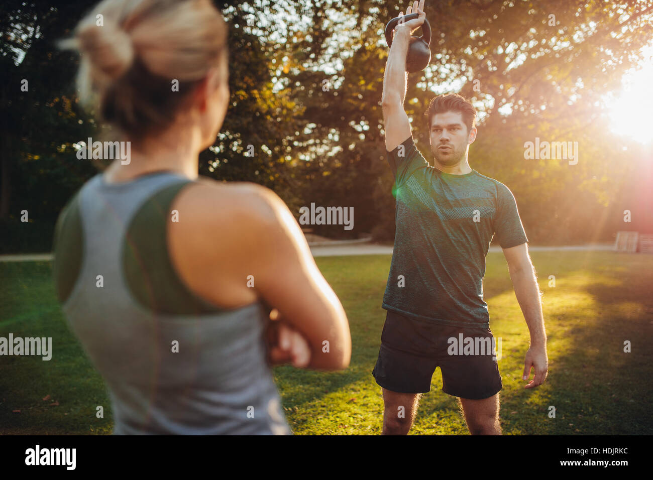 Sano giovane uomo con trainer femmina esercizio con kettlebell nel parco. Montare l'uomo esercita con trainer femmina nella parte anteriore. Foto Stock