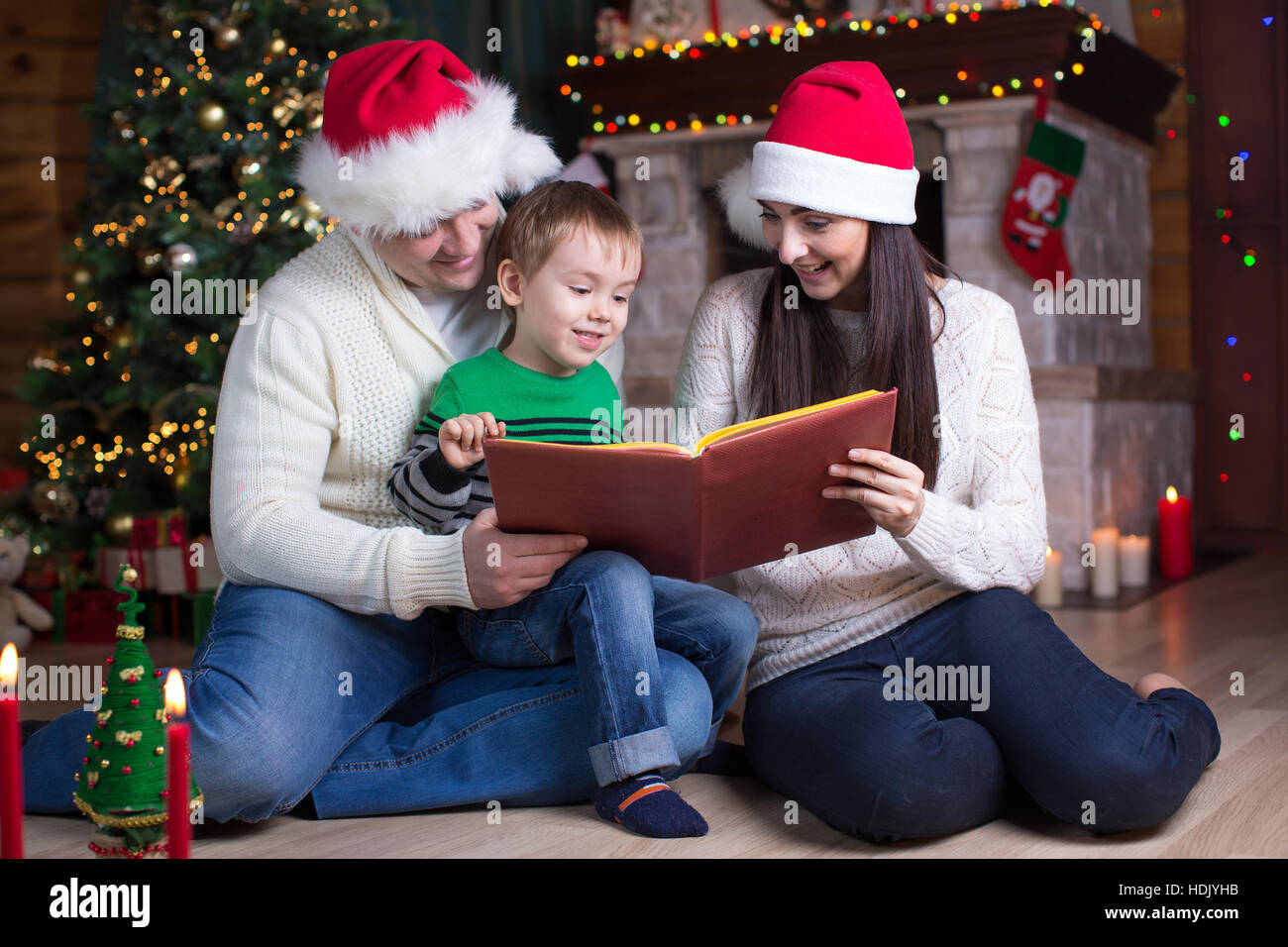 Famiglia, natale, X-mas, concetto - genitori sorridente in cappelli di Babbo Natale e figlio di capretto libro di lettura Foto Stock