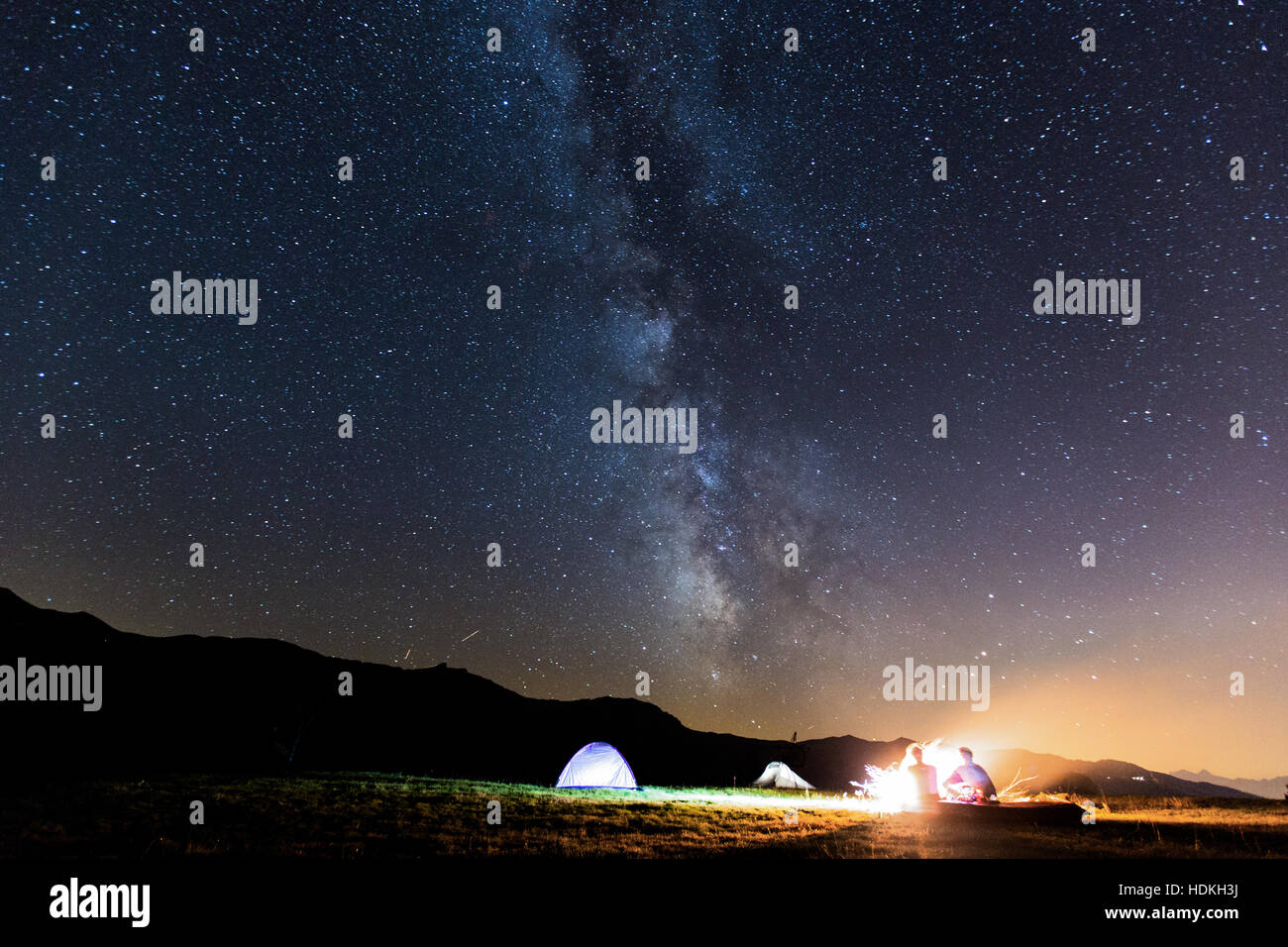 Via Lattea. Cielo notturno con stelle e silhouette di due uomo attorno a un fuoco Foto Stock