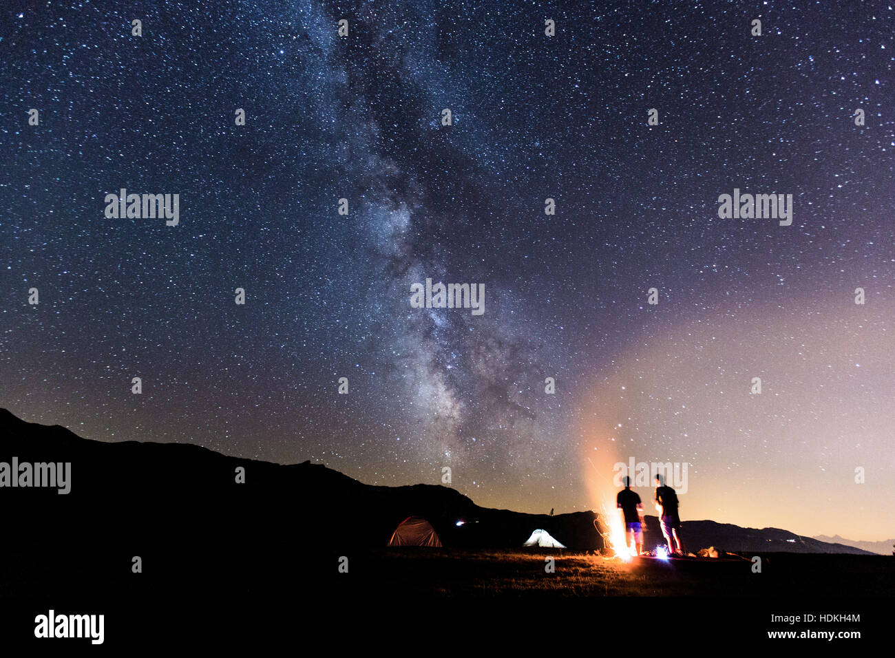 Via Lattea. Cielo notturno con stelle e silhouette di due uomo attorno a un fuoco Foto Stock