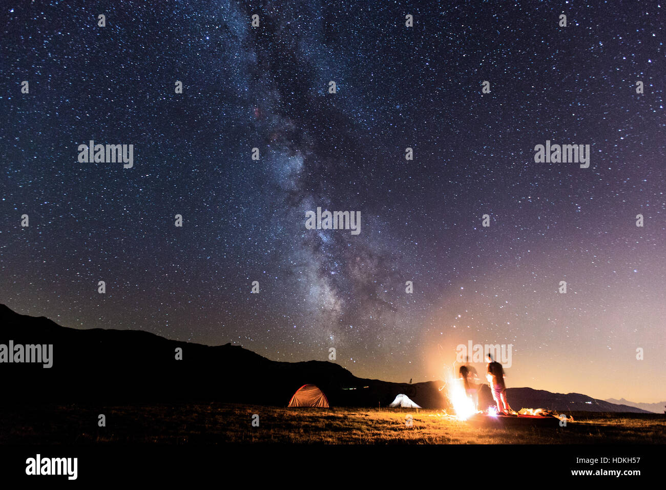 Via Lattea. Cielo notturno con stelle e silhouette di due uomo attorno a un fuoco Foto Stock