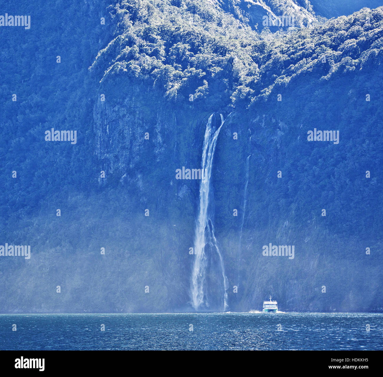 Un turista vele di imbarcazioni passato una cascata di immergersi in Milford Sound nel Fjordland Isola del Sud della Nuova Zelanda Foto Stock