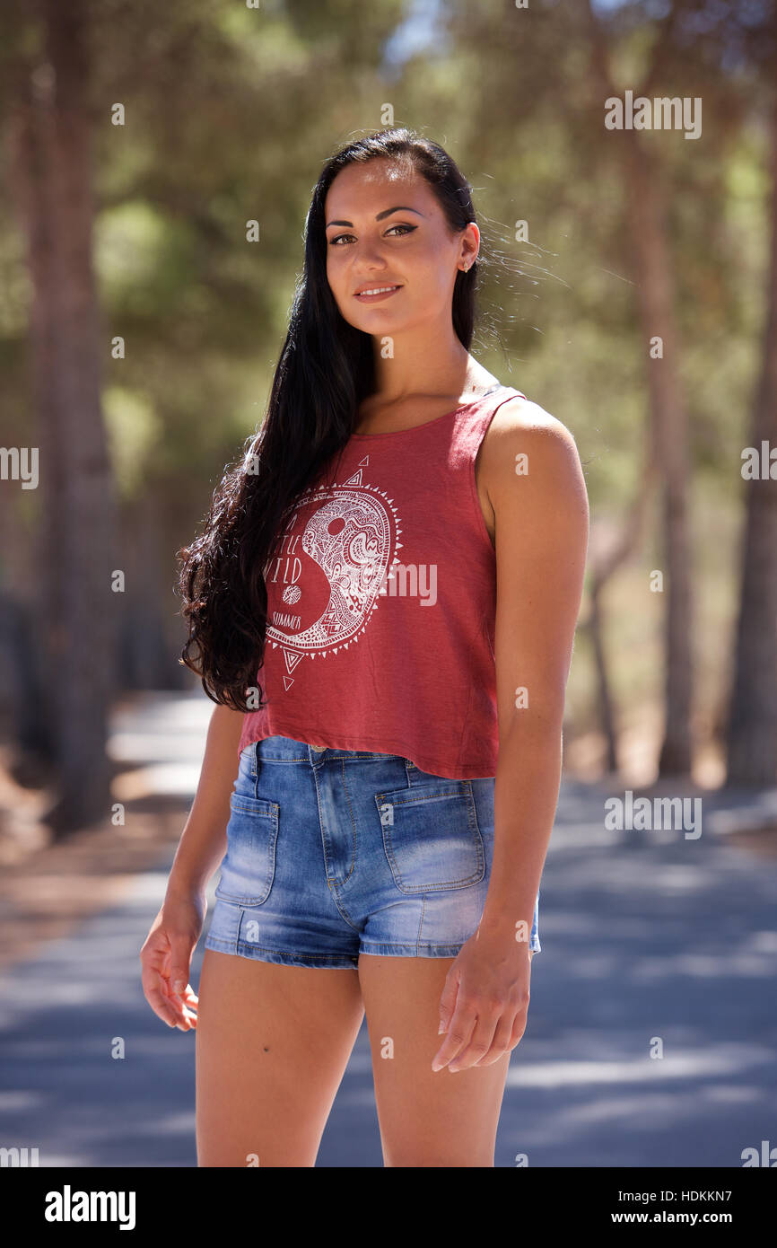 Piuttosto giovane donna con lunghi capelli scuri in pantaloncini corti e gilet rosso, all'esterno. Foto Stock