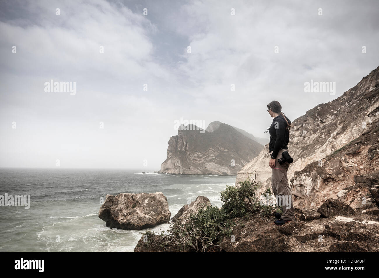 Donna fotografo a guardare il mare da un clif sulla costa di Oman Foto Stock