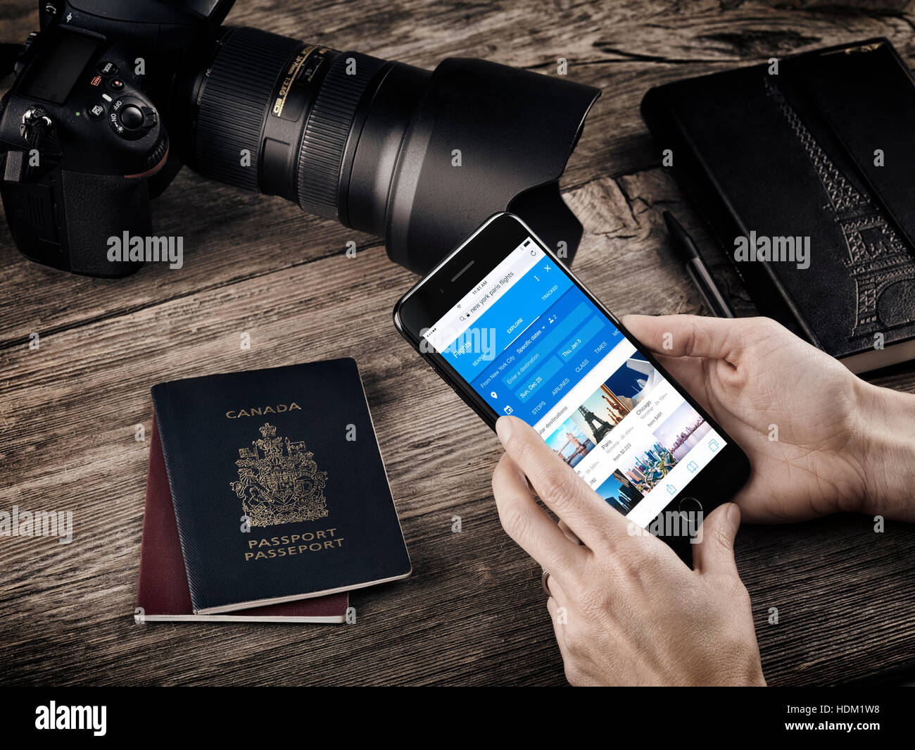 Donna mani con Apple iPhone 7 la visualizzazione di informazioni di volo su una tabella con i passaporti, una fotocamera e un notebook, un viaggio concettuale vita ancora Foto Stock