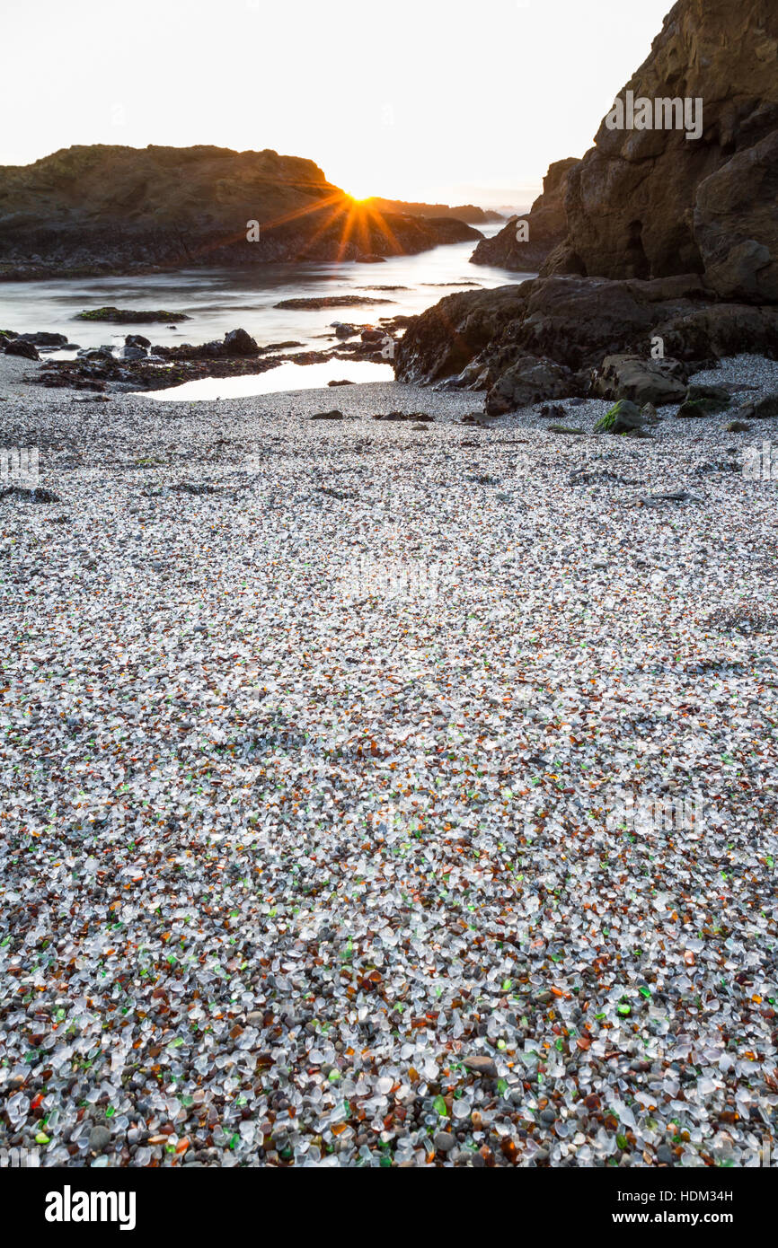 Arancione tramonto sulle rocce dando una luce morbida per i colori del mare di vetro in questa spiaggia Foto Stock
