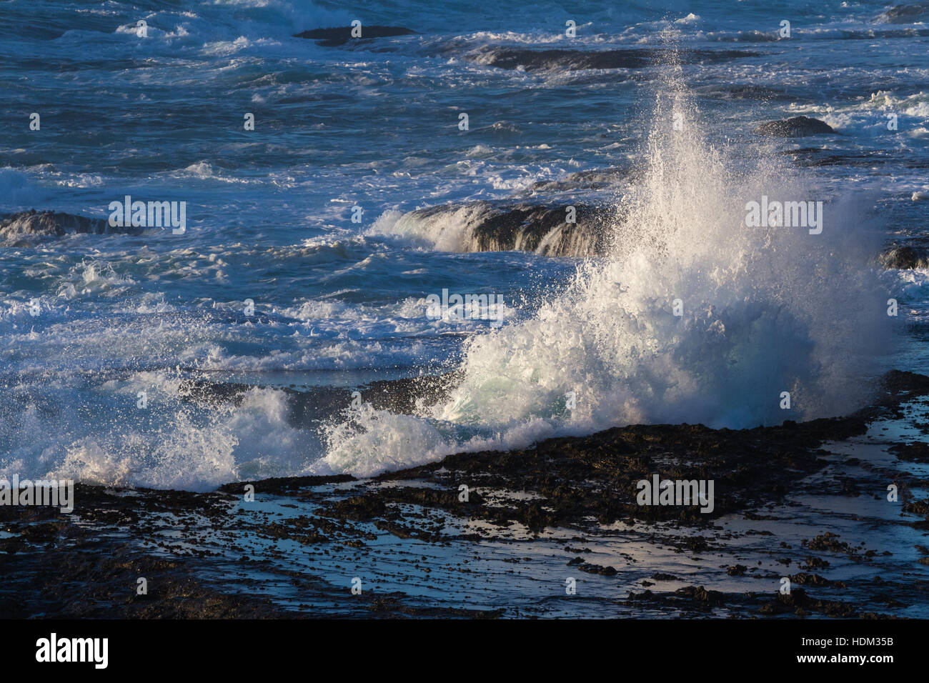 Potente scena con onde che si infrangono creando una drammatica esplosione su questa roccia lavica bluffs Foto Stock