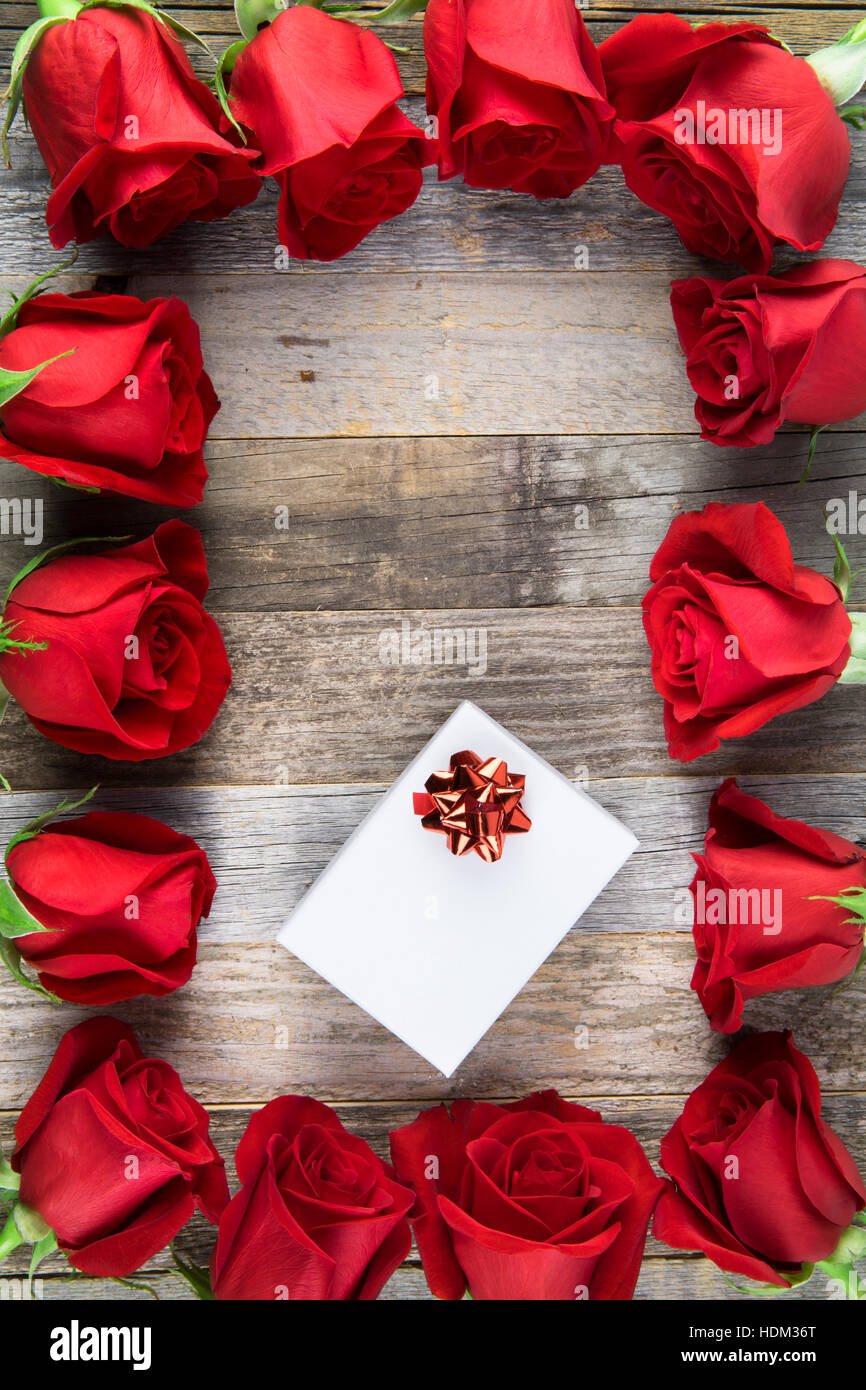 Telaio di rose rosse e scatola regalo bianca su una superficie di legno. Foto Stock