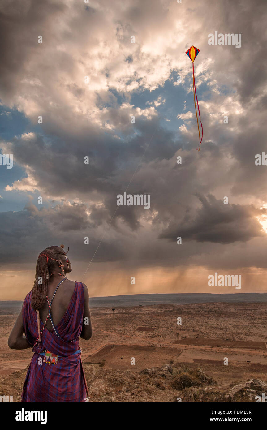 Un guerriero Masai Tribesman volare un aquilone in tradizionali abiti tribali. Kenya, Africa. Vista panoramica. Formato verticale. Foto Stock