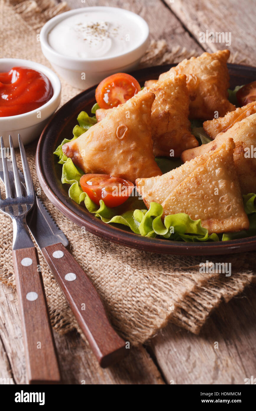 Samosa vegetariani su una piastra con pomodori e lattuga su una tavola di legno verticale. Foto Stock