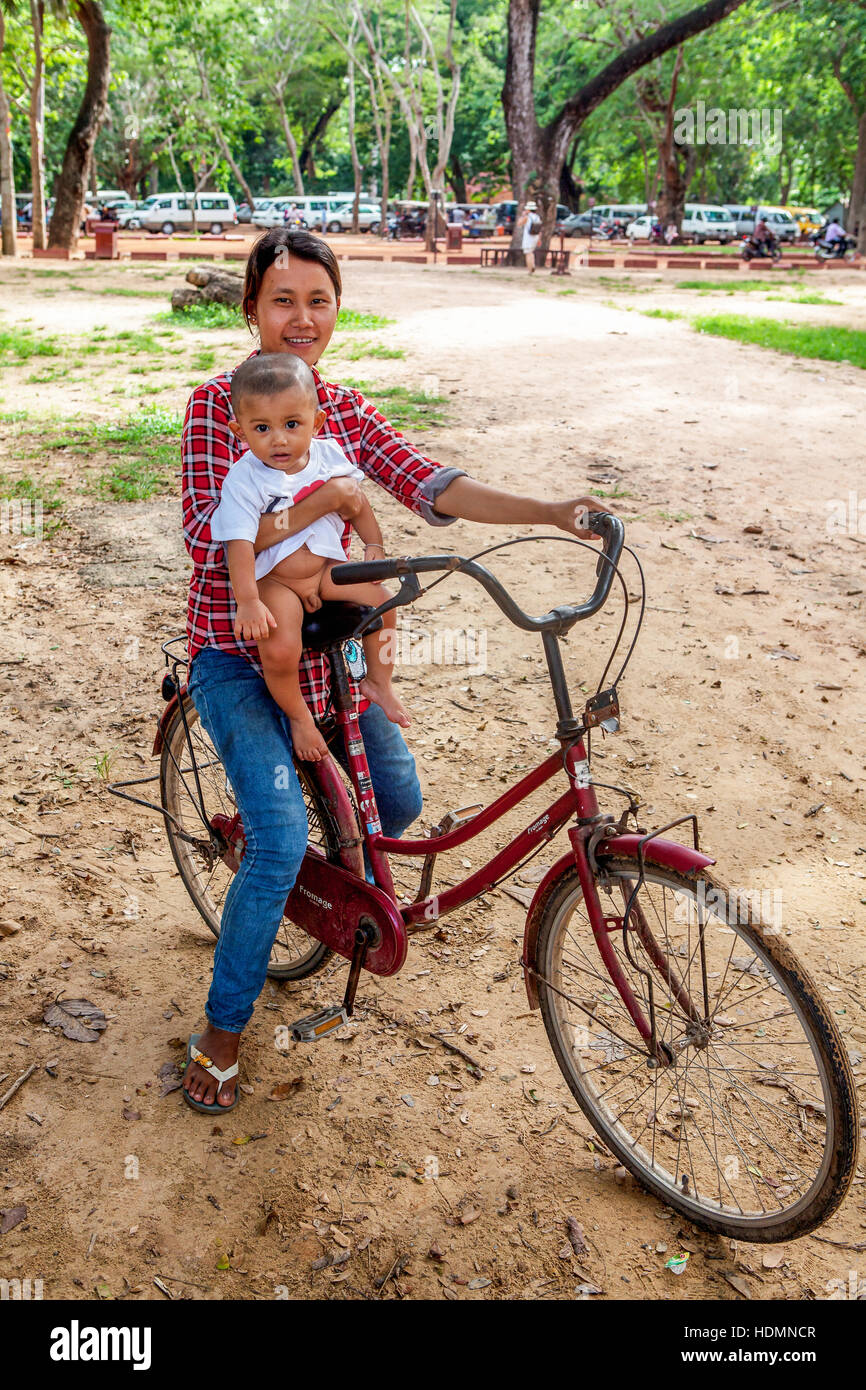 Una giovane madre cambogiano cavalca il suo bambino sul suo rosso, Fromage bicicletta, la più diffusa forma di trasporto in Cambogia. Foto Stock