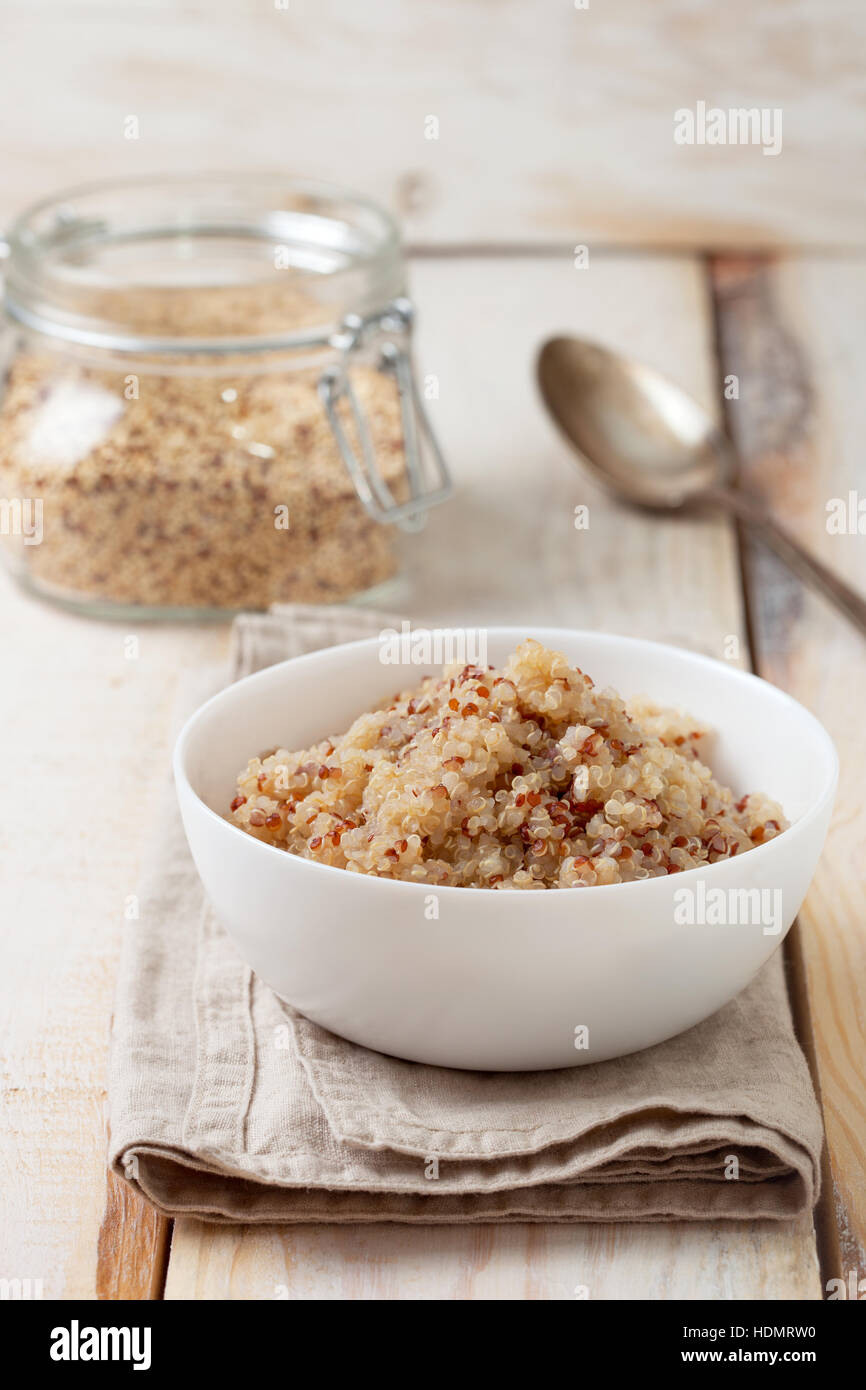 Dieta sana prima colazione. Cuocere la quinoa in una ciotola bianco, la quinoa in un vasetto di vetro su uno sfondo di legno Foto Stock