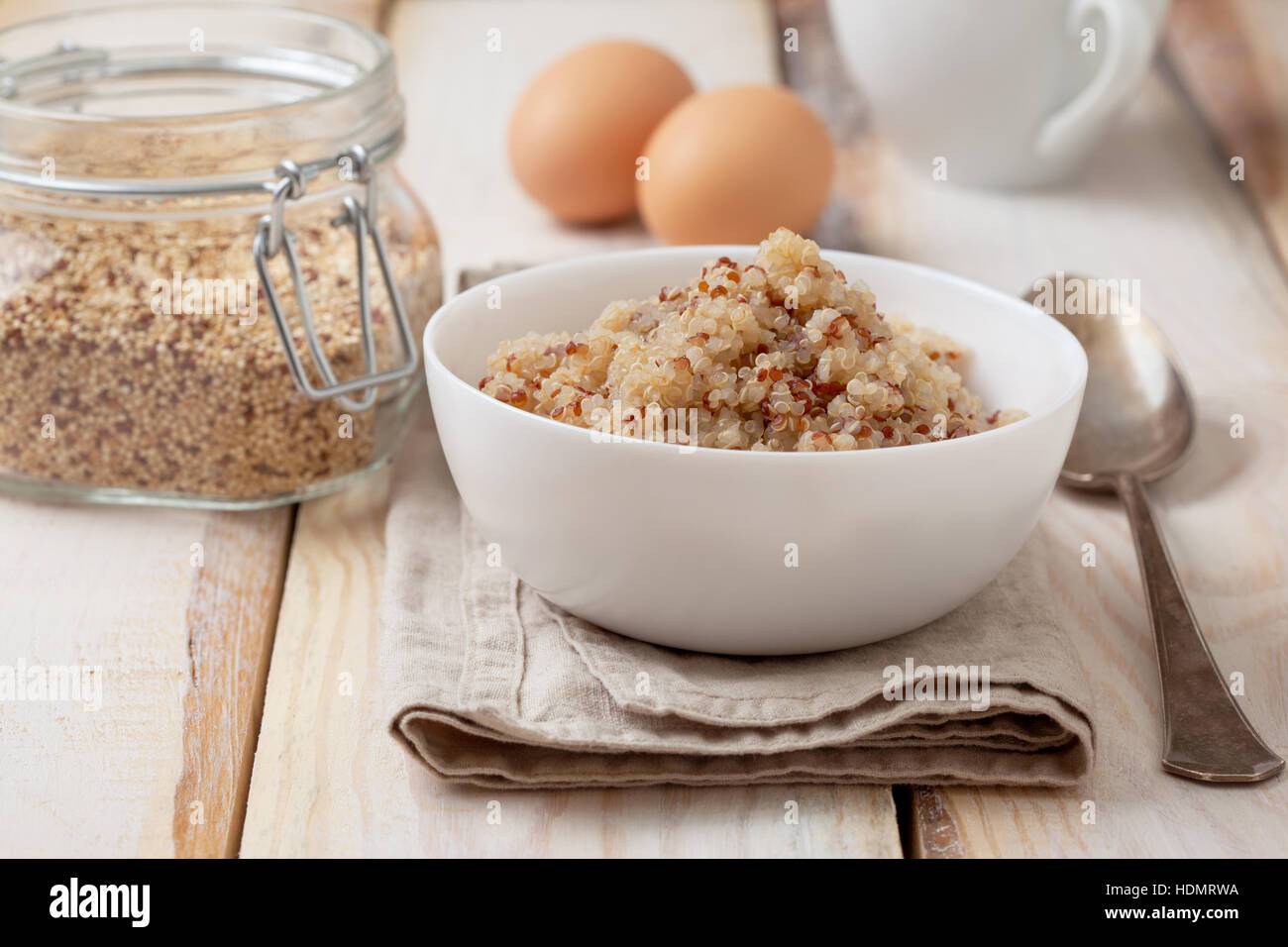 Dieta sana prima colazione. Cuocere la quinoa in una ciotola bianco, uova e una tazza di tè su un sfondo di legno Foto Stock