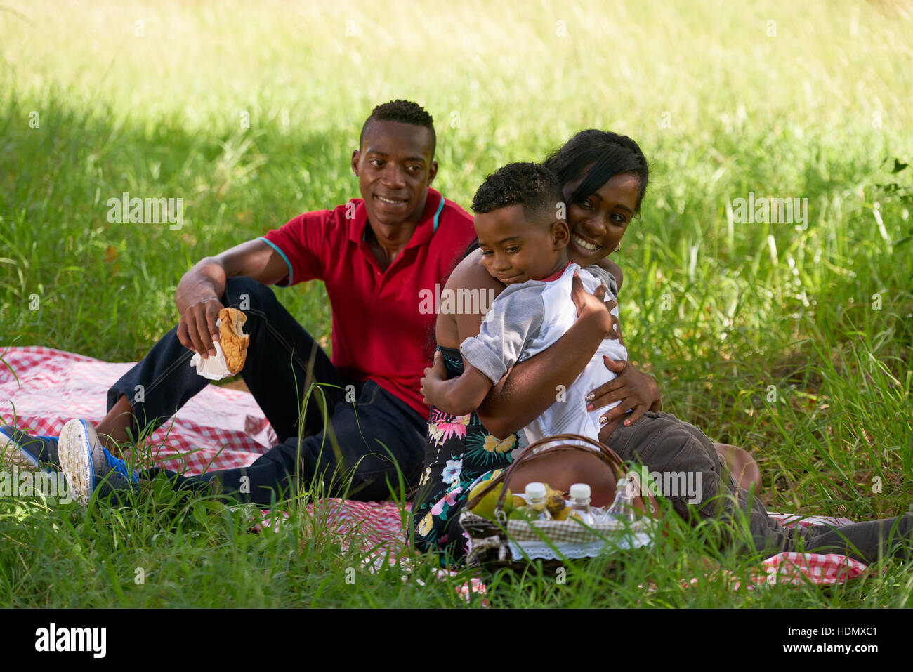 Felice coppia nero con figlio nel parco della città. Famiglia americana africana con un giovane uomo, donna e bambino facendo picnic, avendo divertimento all'aperto. Foto Stock