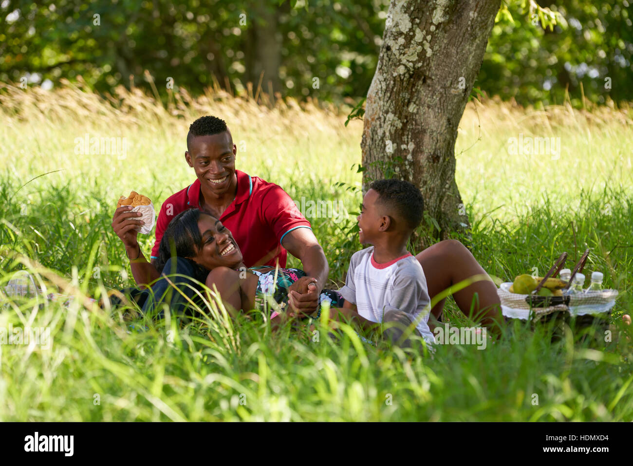 Felice coppia nero con figlio nel parco della città. Famiglia americana africana con un giovane uomo, donna e bambino a mangiare cibo durante un picnic. Foto Stock