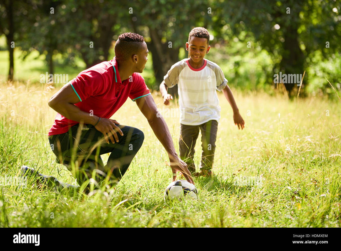 Felice nero di persone facendo pratica di sport nel parco della città. Famiglia americana africana con padre figlio di insegnamento come giocare a calcio. Foto Stock