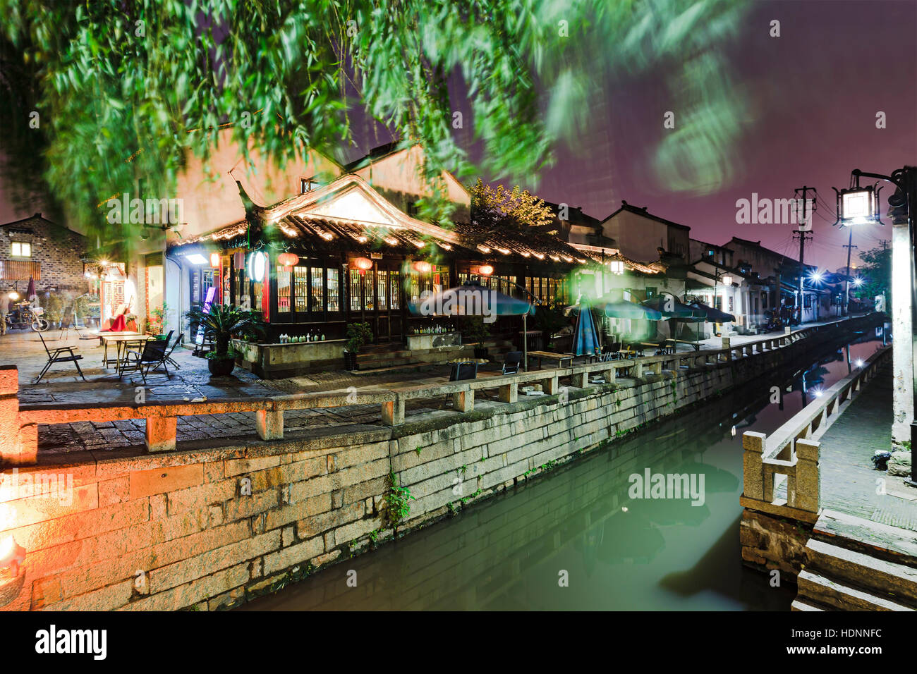 Servizi di vendita al dettaglio e street food caffetterie lungo la strada per lo shopping e canal nell antica Suzhou City downtown al tramonto. Luminose lampade stradali illuminare histor Foto Stock