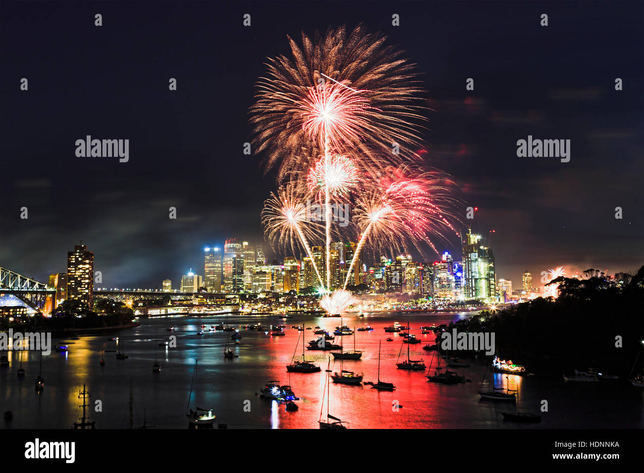 Crescente luce rossa sulla sfera che portano tracce durante il Capodanno fuochi d'artificio a Sydney su city CBD. Luce brillante mostra riflette ancora in acque portuali abo Foto Stock