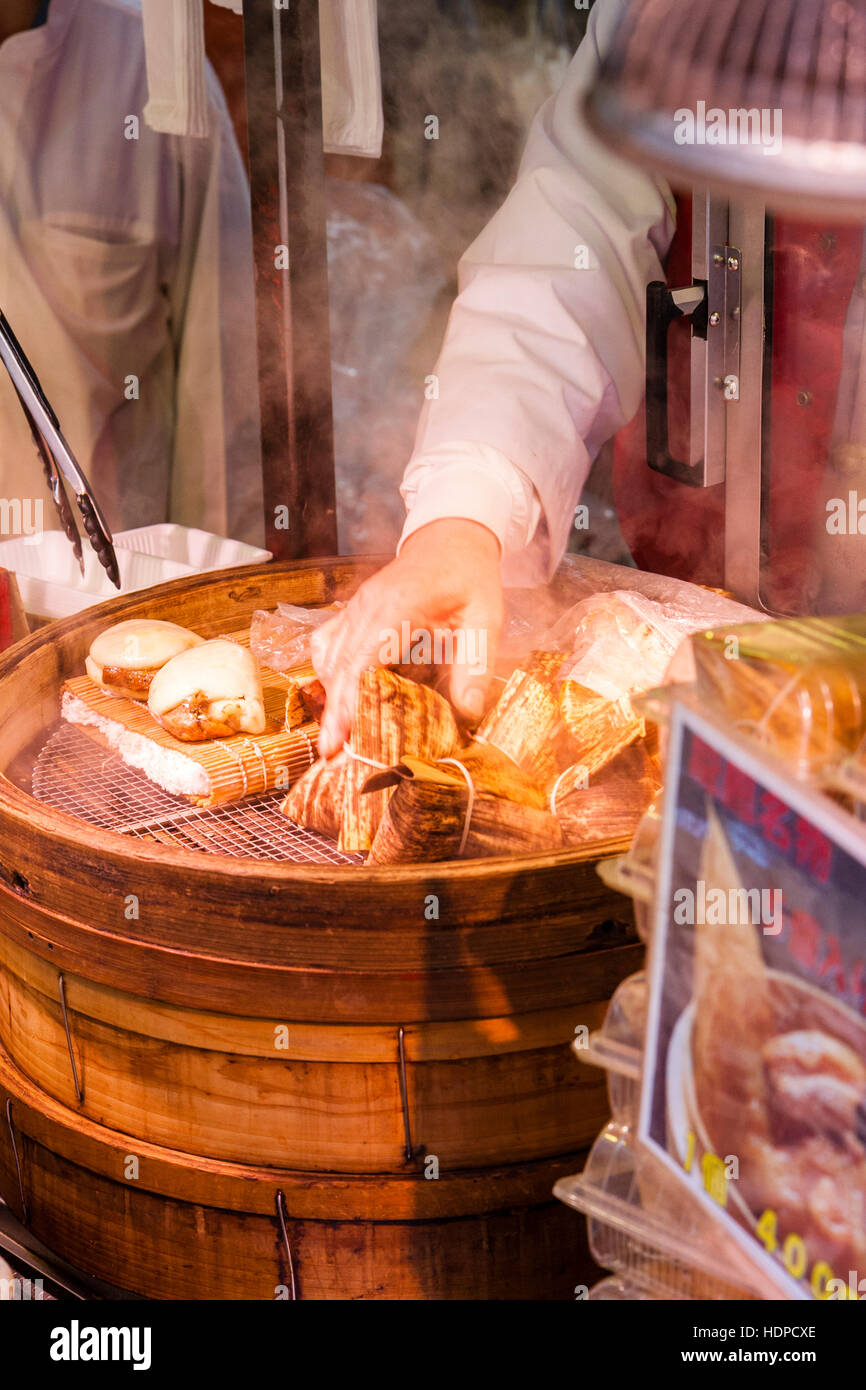 Giappone, Kobe Nankinmachi, Chinatown. Cibo cinese contatore di stallo, pancetta di maiale panini da cuocere in contenitore di legno, con mano girando uno. Foto Stock