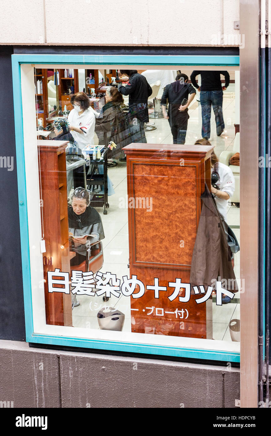 Vista attraverso la finestra incorniciata da un signore giapponese parrucchiere con le donne sedute aventi i loro capelli fatto giapponese kanji script sulla parte inferiore della finestra di . Foto Stock