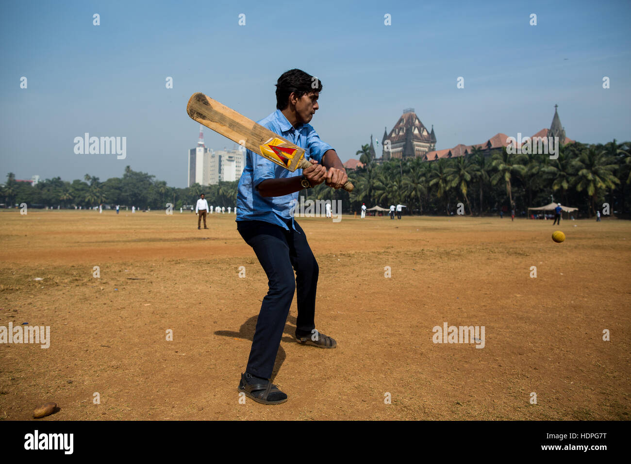 Un uomo indiano gioca il cricket nel centro di Mumbai nella sua ora di pranzo. Foto Stock