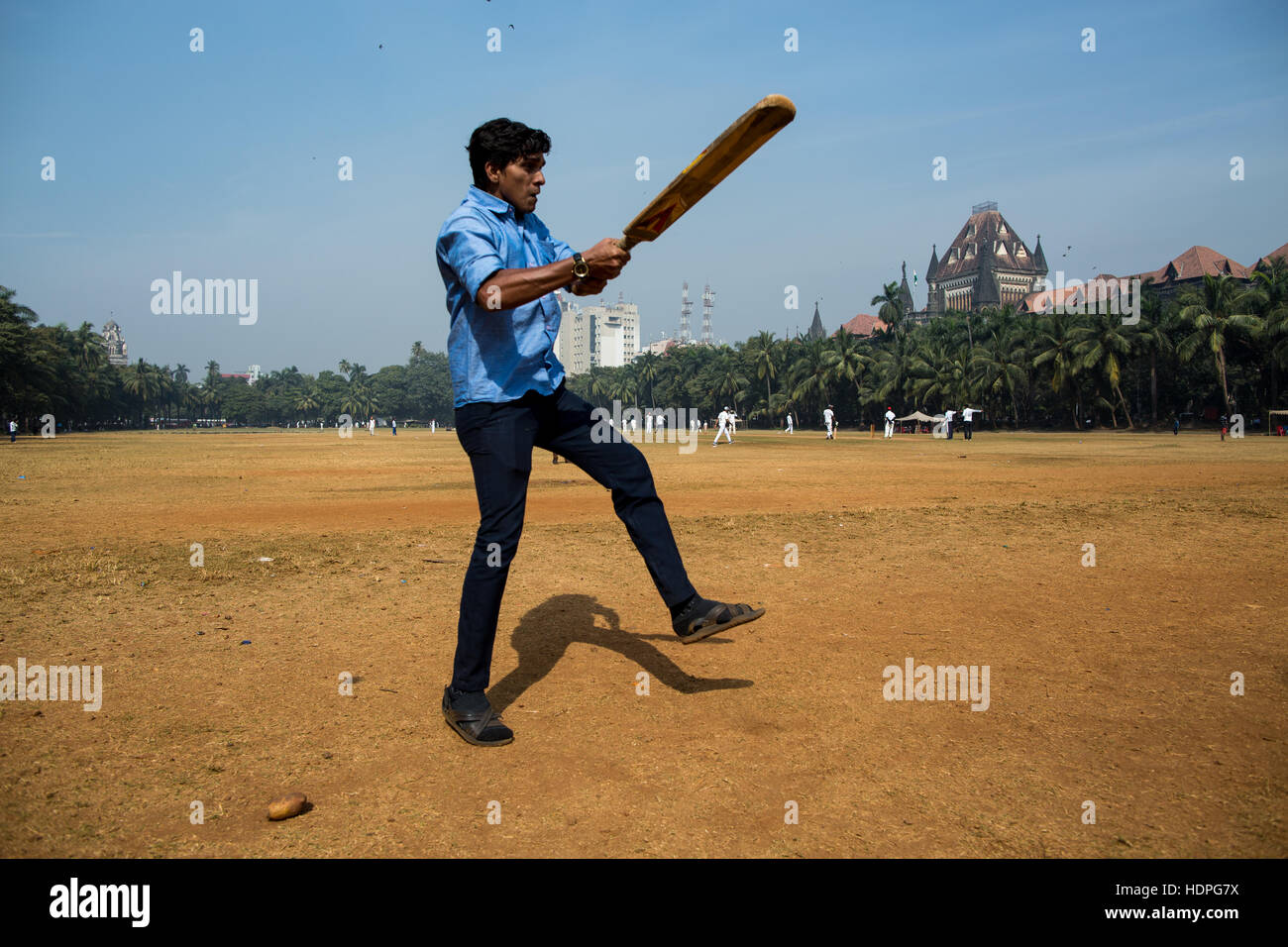 Un uomo indiano gioca il cricket nel centro di Mumbai nella sua ora di pranzo. Foto Stock