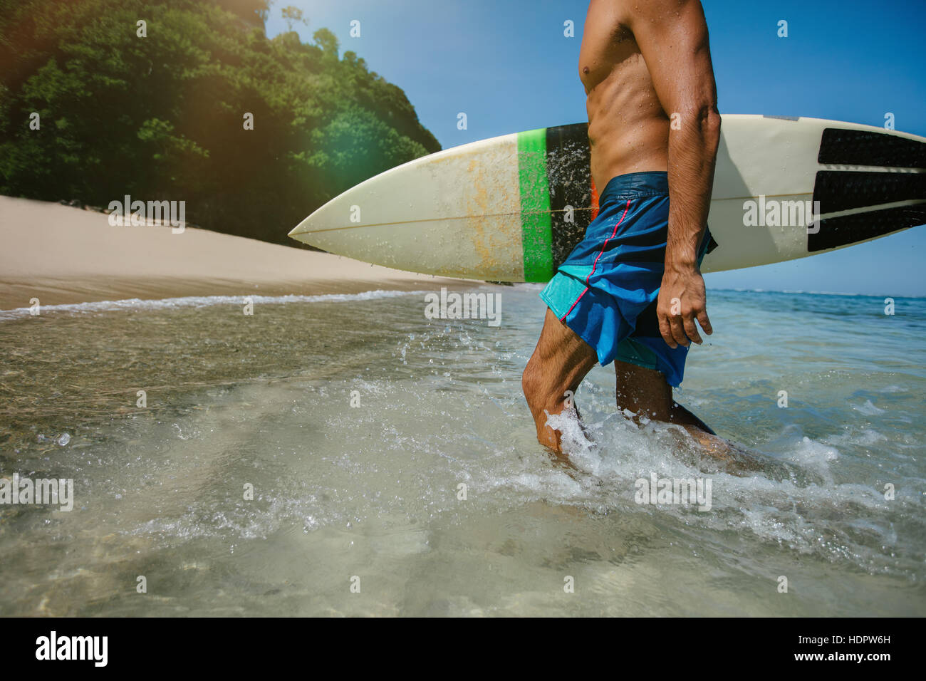 Ritagliato colpo di giovane maschio surfer tenendo tavole da surf a piedi dell'oceano. Maschio caucasico con tavola da surf proveniente dal mare. Foto Stock
