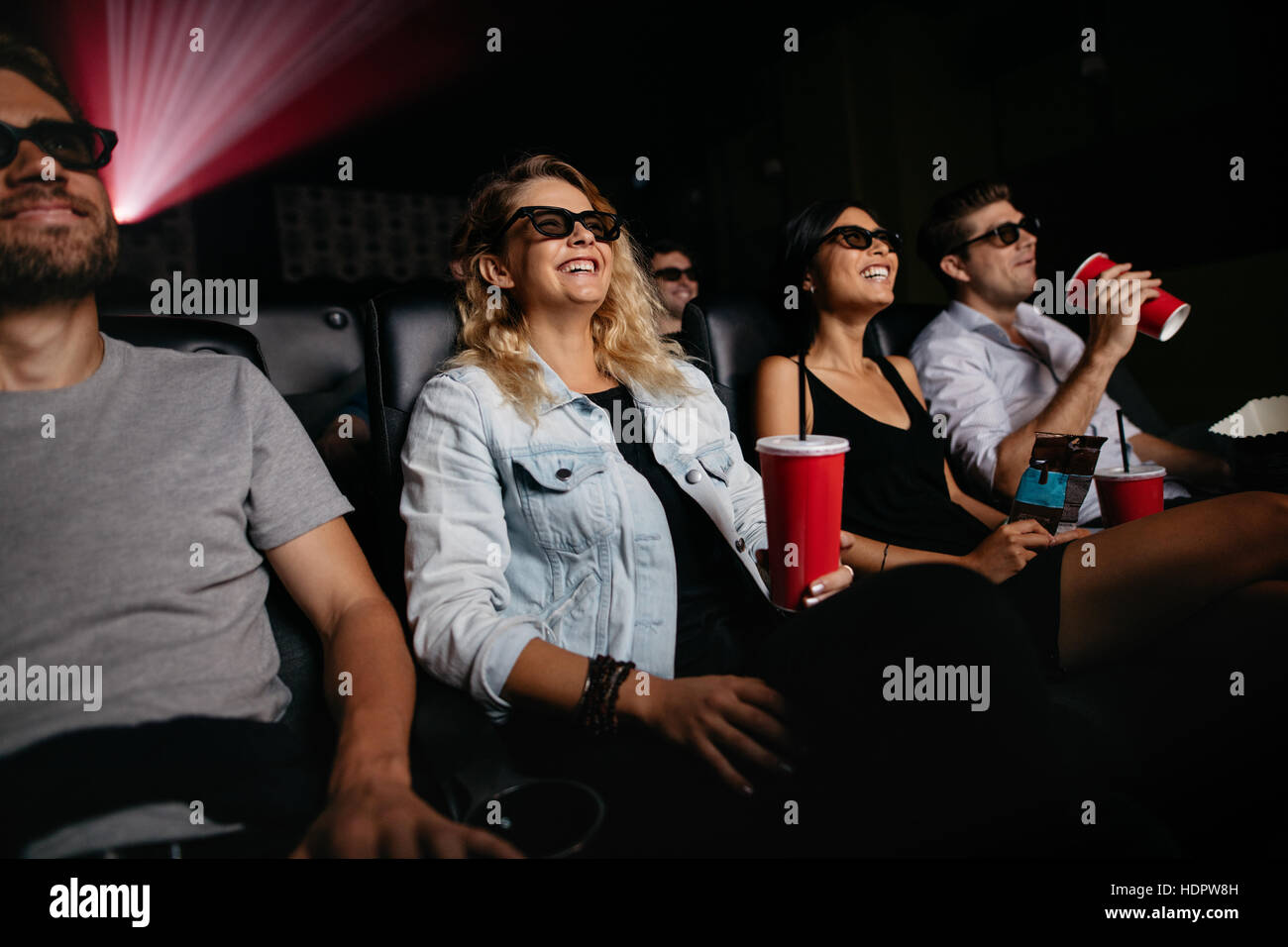 Giovani donne e uomini la visione di film in 3D nei cinema. Gruppo di persone a teatro con occhiali 3d e bevande. Foto Stock