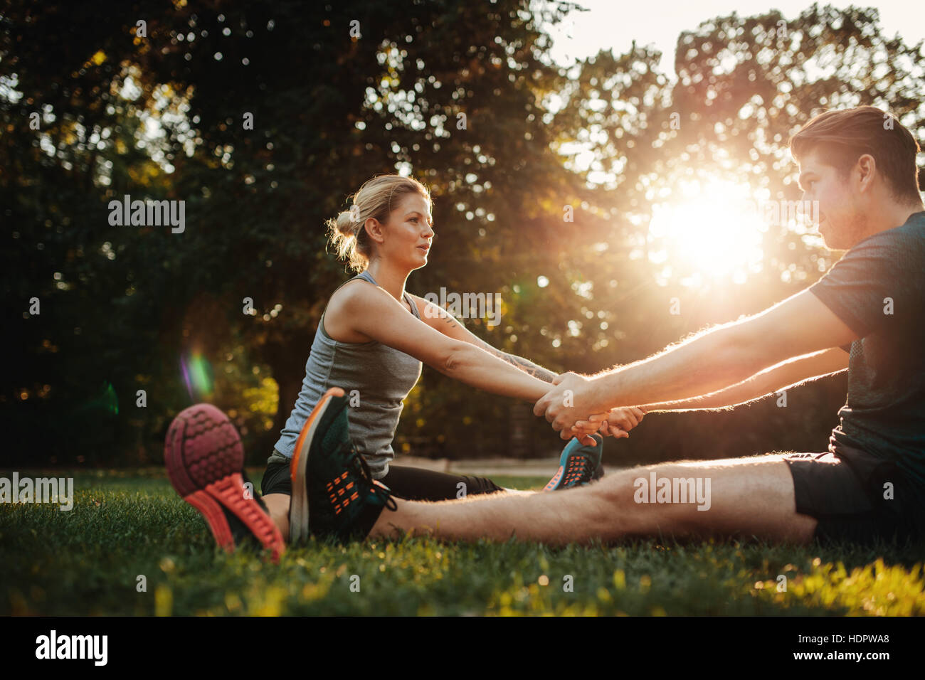 Sano giovane uomo e donna che esercitano nel parco. Sorridente coppia caucasica tenendo le mani e lo stiramento in mattina. Foto Stock