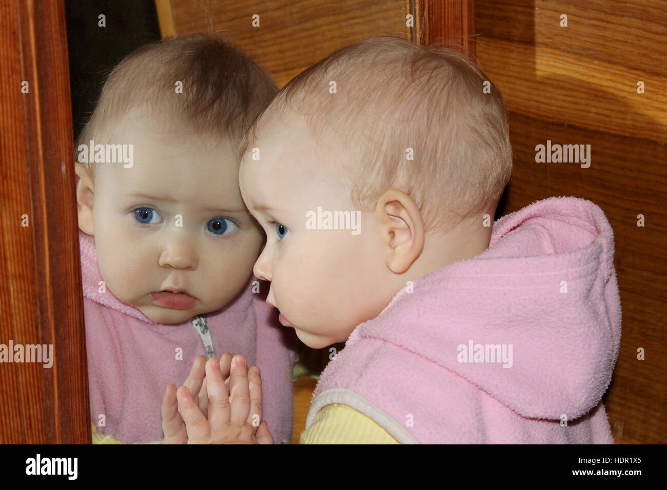 Divertenti baby guarda se stessa nella parte anteriore dello specchio Foto Stock