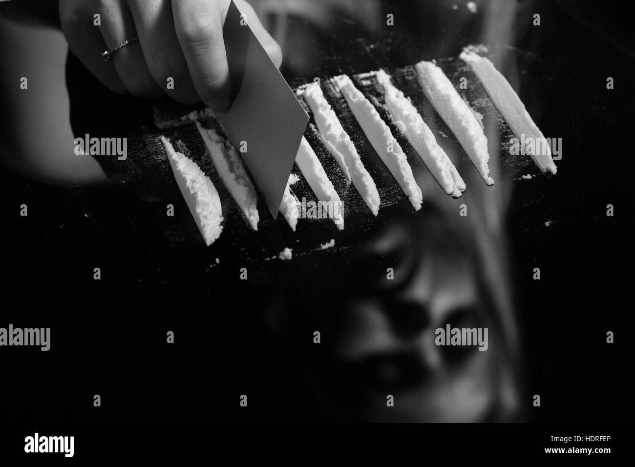 La cocaina o altre droghe tagliato con la carta sullo specchio di riflessione femminile, mano dividendo polvere bianca narcotico, monocromatico Foto Stock