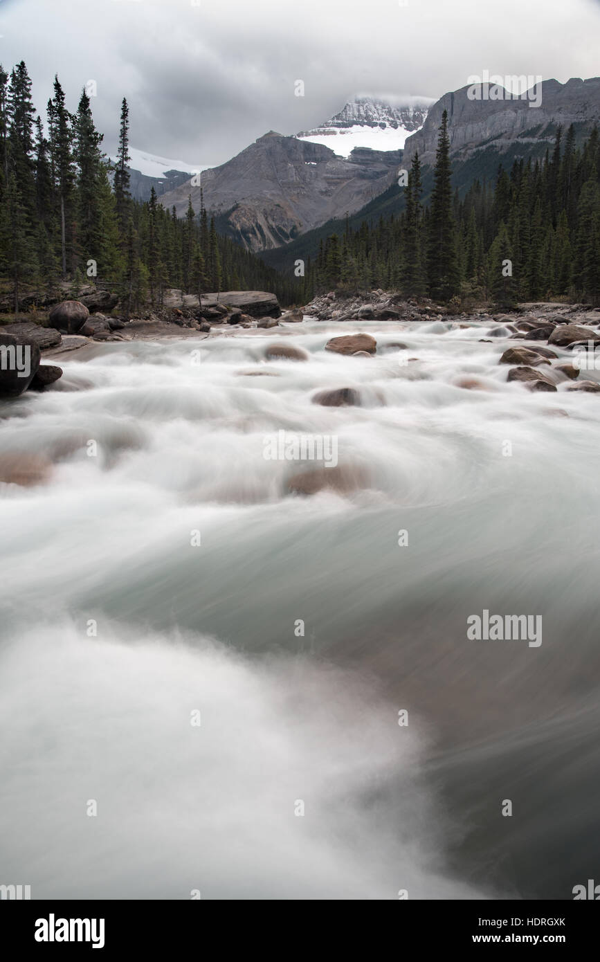 In rapido movimento di acqua che fluisce oltre le rapide con le Montagne Rocciose Canadesi in background Foto Stock